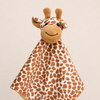 A plush giraffe security blanket with a brown and white spotted pattern, featuring a smiling face and ossicones, set against a solid light beige background.