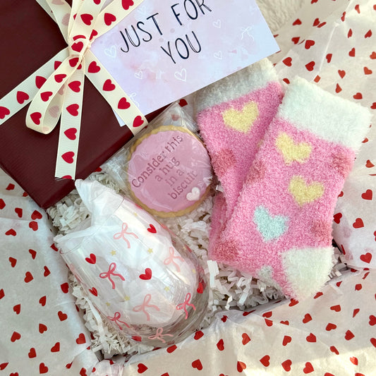 Gift set with pink heart-patterned socks, cookies, heart and bow design wine glass and a card in heart tissue paper. Hearts & Bows | Gift For Her