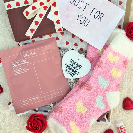 Love and hearts themed gift box including a face mask, heart-patterned socks, and a love you to the moon and back ceramic heart. 