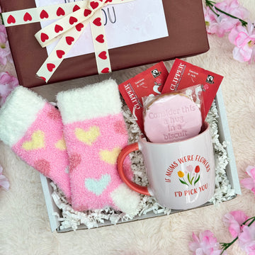 Sips, Socks & Smiles | Mother's Day Gift. Gift set with pink heart-patterned socks, mug, and cookie in a box.